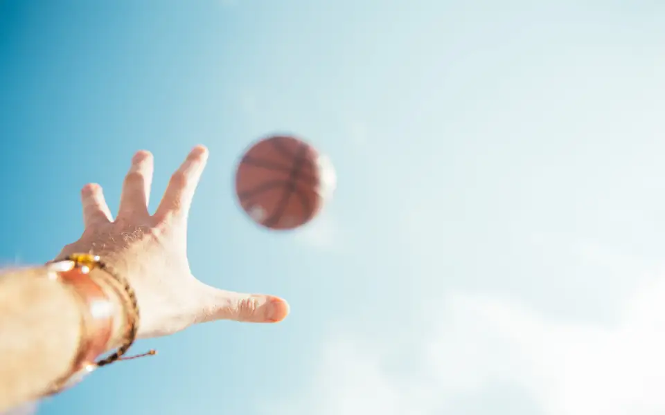 Hand releasing a basketball shot against a blue sky, for JLBETPH PBA and NBA betting